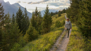 Mature woman walks down trail in the morning in mountains as if looking for inspiration