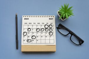 Calendar on daesk with pen, glasses and small plant-holidays are marked with a circle