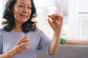 Close-up of a happy senior lady holding a glass of water and taking a pill. The smiling elderly woman is using supplements.