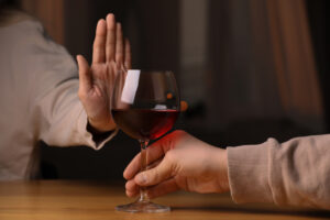 Woman's hand up, refusing to drink red wine indoors, closeup.