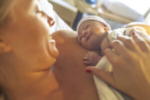 Mother with newborn baby son lying in bed, smiling at each other