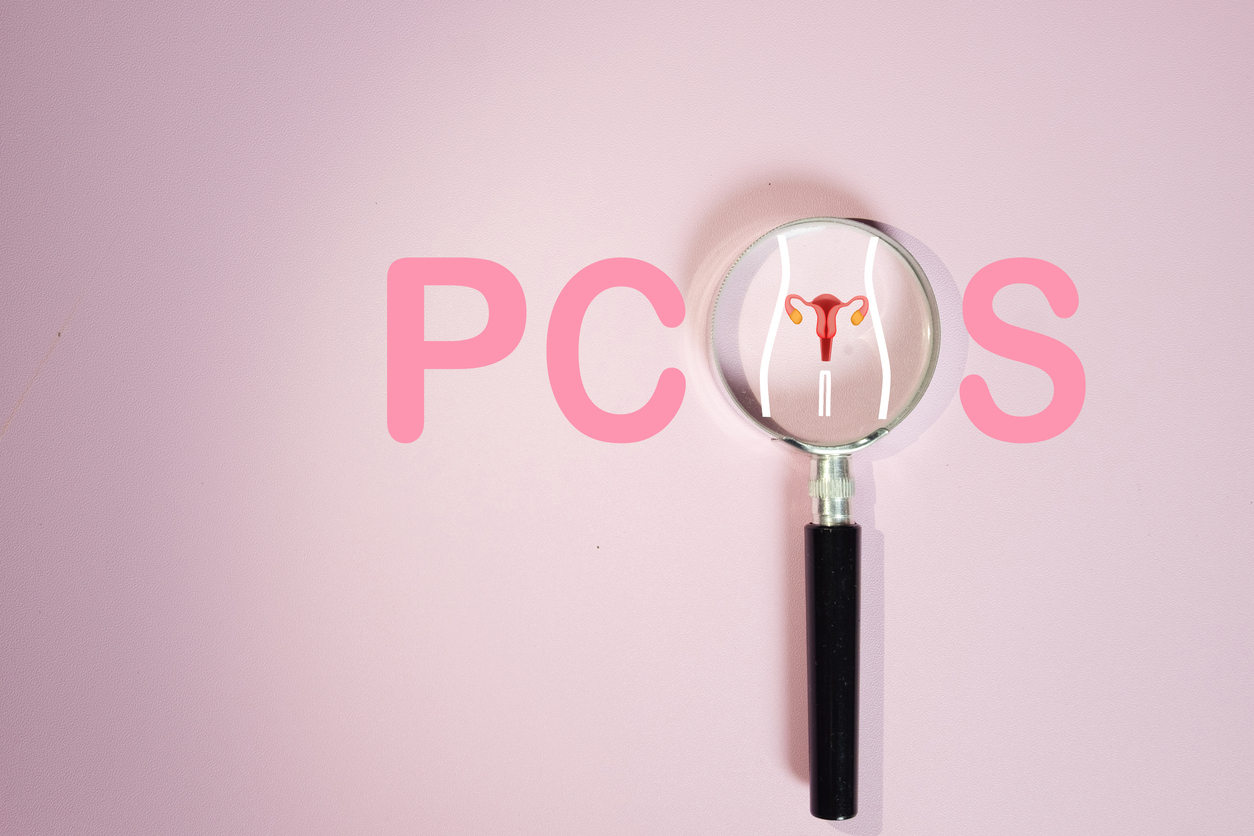 PCOS (Polycystic Ovary Syndrome) diagnosis and awareness concept; letters on pink background, with a magnifying glass for the O and a uterus diagram under the glass.