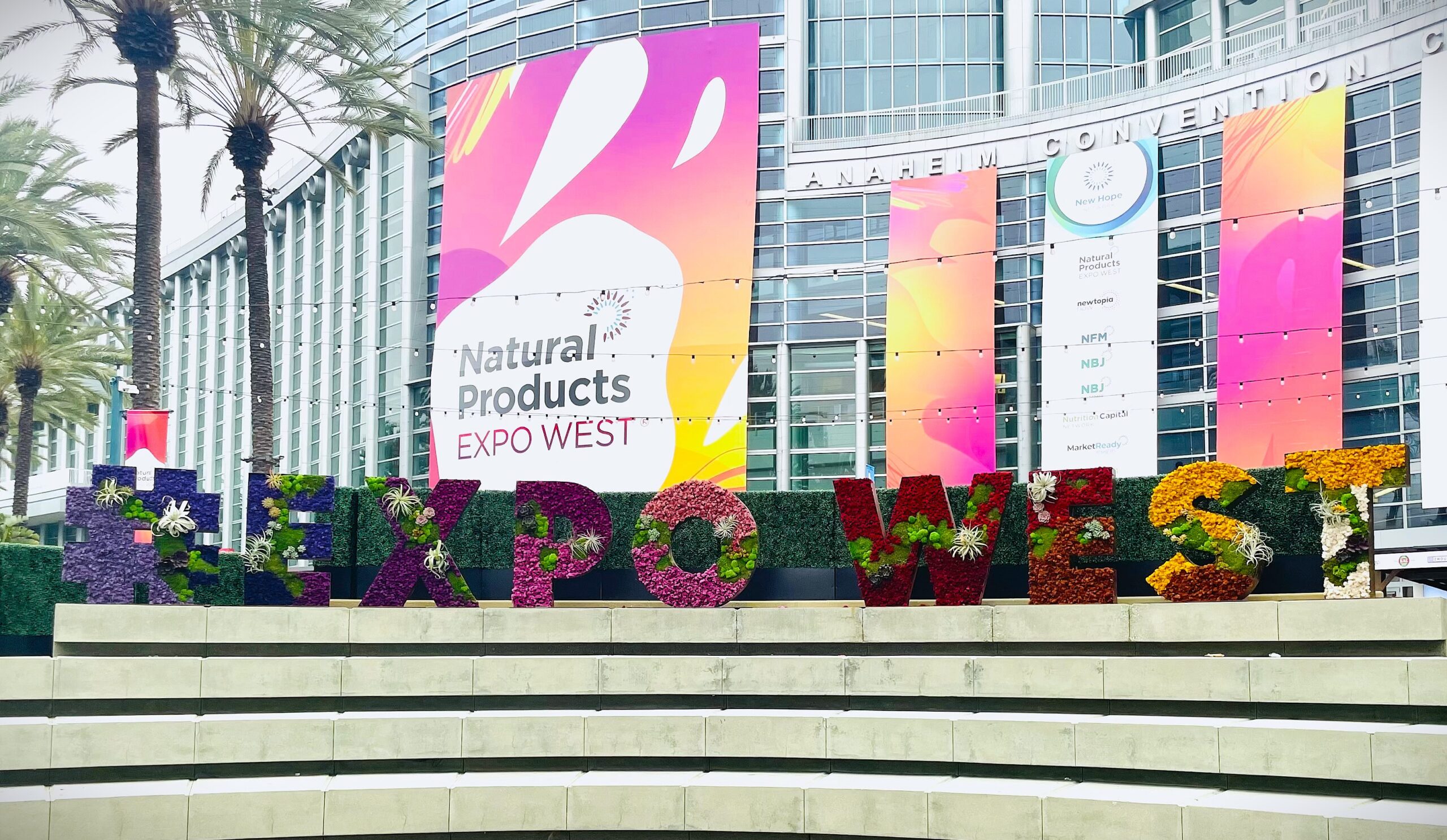 Image of the entrance to Expo West, with large banners and a floral design atop the steps of the front entrance